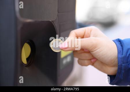 Ritratto ravvicinato di una mano di donna che usa una moneta per pagare il parchimetro Foto Stock