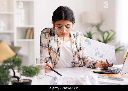 Una giovane ragazza indiana stanca si arrabbia per il numero di compiti, sbriciola la carta e la getta via, cerca di calmarsi meditando. Stressante Foto Stock