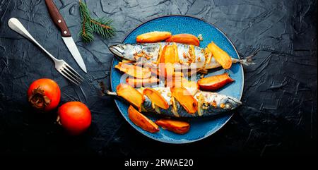 Pesce cucinato con marinata di frutta di cachi su un tavolo da cucina in cemento. Pesce intero al forno, sgombro. Vista dall'alto. Foto Stock