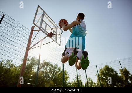 Un teenager che lancia palla nel canestro da basket, tira in movimento Foto Stock