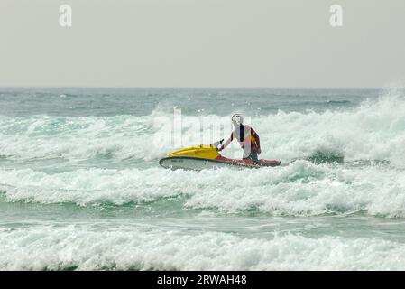 Membro del bagnino RNLI in mare aperto al largo di Perranporth Beach, Cornovaglia, Regno Unito. Operatore di imbarcazioni di soccorso che cavalca in mare Foto Stock