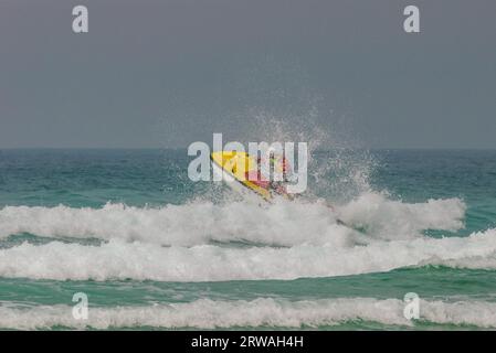 Membro del bagnino RNLI a bordo di Jetski che si dirige verso i mari mossi al largo di Perranporth Beach, Cornovaglia, Regno Unito. Operatore di imbarcazioni di soccorso che si dirige verso il mare Foto Stock