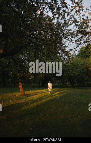 Vista posteriore di una donna con un pantaloni bianco che cammina attraverso un parco in estate, Bielorussia Foto Stock