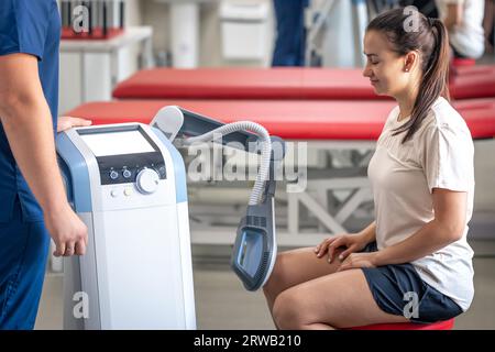 Medico che utilizza la macchina per trattare le articolazioni del ginocchio di un paziente. Foto Stock