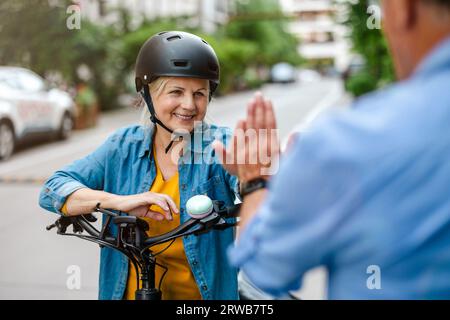 Donna matura sorridente in casco che dà cinque in alto all'uomo mentre si va in bicicletta Foto Stock