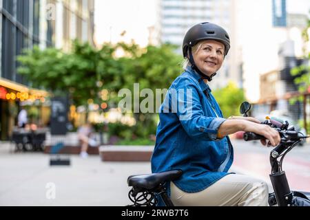 Ritratto di una donna anziana che indossa il casco mentre si va in bicicletta in città Foto Stock