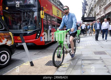 Londra, Regno Unito. Uomo che pedala sul marciapiede di Piccadilly su una bici a noleggio Lime Foto Stock