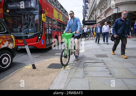 Londra, Regno Unito. Uomo che pedala sul marciapiede di Piccadilly su una bici a noleggio Lime Foto Stock