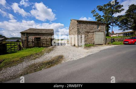 Una soleggiata giornata di agosto e due edifici costruiti in pietra sorgono su ogni lato di una pista agricola che conduce ai campi di Halton East Foto Stock