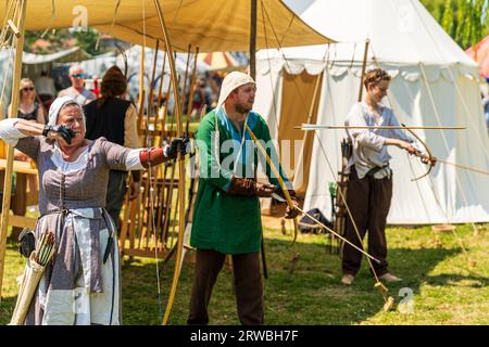 Rievocazione medievale con una donna in costume d'epoca, sparando un arco e una freccia con la freccia a metà volo, mentre due uomini dietro di lei preparano i loro archi. Foto Stock