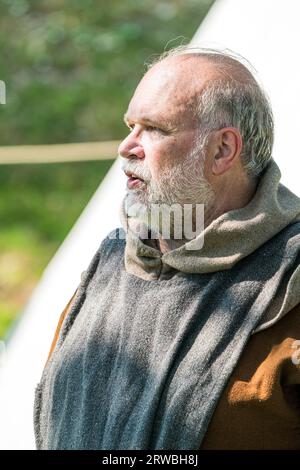 Un uomo vestito da frate, monaco o sacerdote medievale durante una rievocazione. Vista laterale dell'uomo, con accappatoi grigi e marroni e barba grigia. Foto Stock