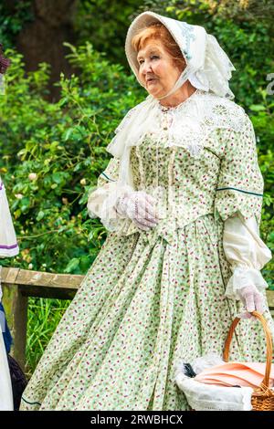 Donna anziana vestita in costume del periodo vittoriano con un abito verde e un cofano con uno scialle di pizzo, in piedi in un giardino. Broadstairs Dickens Week. Foto Stock