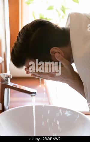 Giovane che lava il viso con acqua, la routine del mattino Foto Stock