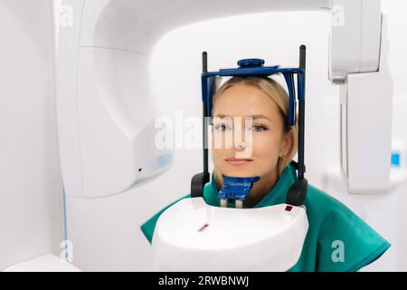 Vista frontale di una giovane paziente in piedi in una macchina a raggi X dentale per radiografia dentale in una clinica odontoiatrica moderna. Concetto di odontoiatria Foto Stock