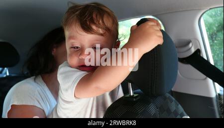 Madre che tiene il bambino in auto sul sedile posteriore senza protezione, piangendo il bambino Foto Stock