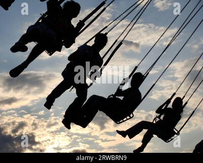 La gente cavalca su una giostra. Sagome di persone che cavalcano su una giostra al tramonto. Foto Stock