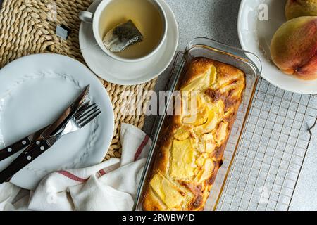 Vista dall'alto della torta di pesca stagionale servita su una griglia da forno vicino al piatto con forchetta e coltello e una tazza di tè posta sul tavolo vicino al tovagliolo Foto Stock