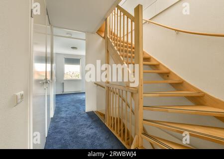 Corridoio con pavimento in moquette blu e pareti bianche con scala in legno che conduce al piano superiore in una casa moderna Foto Stock