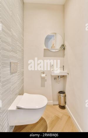 Interni di un bagno contemporaneo con WC e specchio circolare sopra il lavandino e rotolo di carta su parete bianca in una casa moderna Foto Stock