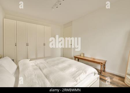 Gli interni di una camera da letto moderna con comodo letto bianco con piumone e cuscini contro il guardaroba bianco in uno spazioso appartamento Foto Stock