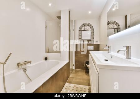 Interno di un elegante bagno luminoso con vasca in ceramica bianca e lavandino con specchio su pareti bianche in una casa contemporanea Foto Stock