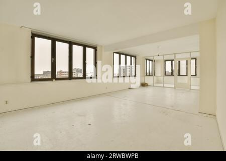 Gli interni di una spaziosa camera vuota con grandi finestre e specchio con riflesso si trovano in un moderno appartamento con pareti e pavimento Foto Stock