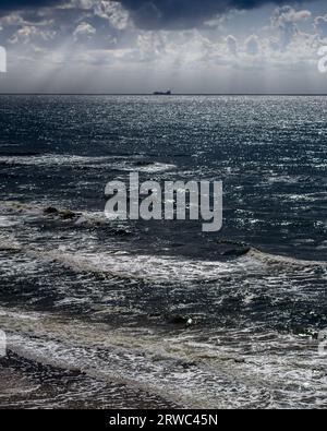 Mar Baltico, a mezzogiorno, i raggi del sole si infrangono tra le nuvole e una nave all'orizzonte Foto Stock