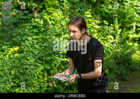 Giovane ragazza nella foresta che legge una mappa e cerca un punto di controllo. Gara di orientamento sportivo. Atleta adolescente che si sposta verso il punto di controllo Foto Stock