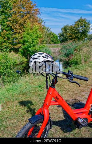 Wassmannsdorf, Germania - 17 settembre 2023: Bicicletta rossa parcheggiata con casco da bicicletta sul manubrio di fronte alla vegetazione. Foto Stock