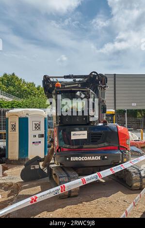 Viladecans, Spagna - 18 settembre 2023: WC temporaneo portatile in plastica per lavori di costruzione sulla strada accanto a una macchina da escavatore. Foto Stock