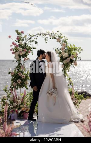 Splendida sposa e sposo durante una cerimonia nuziale all'aperto su una spiaggia vicino al mare. Luogo perfetto Foto Stock