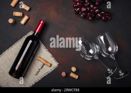 Bottiglia di vino, due bicchieri, uva rossa, cavatappi e tappi, vista dall'alto su sfondo arrugginito, spazio per copiare Foto Stock