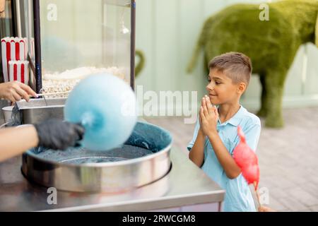 Un ragazzo che aspetta una dolce caramella di cotone al parco divertimenti Foto Stock