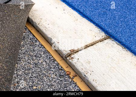 Marciapiede in calcestruzzo accanto a una pista da corsa e chiodatrice in legno per il fissaggio di tappeti erbosi sintetici Foto Stock