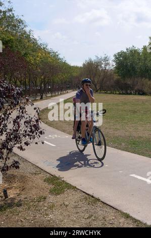 Viladecans, Spagna - 18 settembre 2023: Padre ciclista con sua figlia irriconoscibile seduta dietro sulla pista ciclabile nel mezzo di un parco pubblico Foto Stock