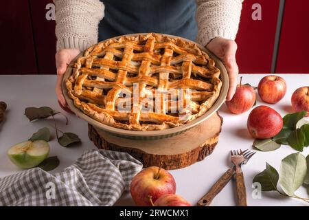 Donna che tiene in mano e mostra una gustosa torta di mele cotta pronta per essere messa in forno. Preparazione della crostata del Ringraziamento, panetteria autunnale. Dolci croccanti per il tempo. Foto Stock