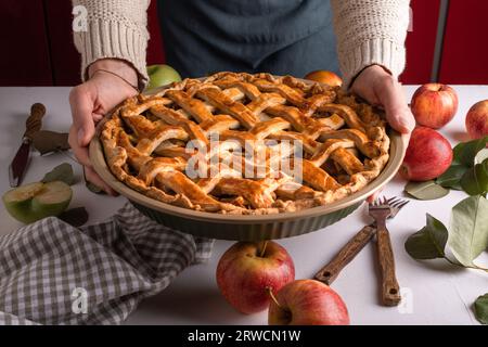 Donna che tiene in mano e mostra una gustosa torta di mele cotta pronta per essere messa in forno. Preparazione della crostata del Ringraziamento, panetteria autunnale. Dolci croccanti per il tempo. Foto Stock