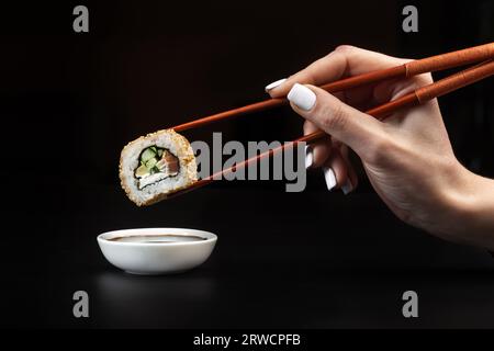 Tenere il sushi sulla ciotola con la salsa di soia sul tavolo nero. Foto Stock