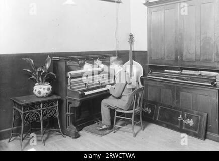 Un cieco che sintonizza un pianoforte verticale, con un violoncello nell'angolo alla sua destra. 5 settembre 1912. Fotografo sconosciuto. Foto Stock