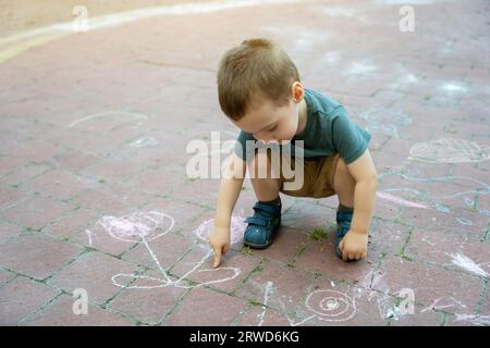 Il bambino di due o tre anni punta il dito sui disegni dei bambini disegnati in gesso. Tempo di gioco per bambini. Giochi per bambini. Selettivo Foto Stock