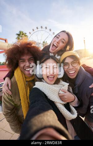 Gruppo di amici multirazziali eccitati in verticale che scattano selfie divertenti che sembrano sorridere alla fotocamera. Foto Stock