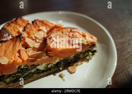 Vista dall'alto, tonalità moody, una fetta di torta di patate dolci e spinaci, un piatto e un tavolo in legno sotto la luce del sole. Foto Stock