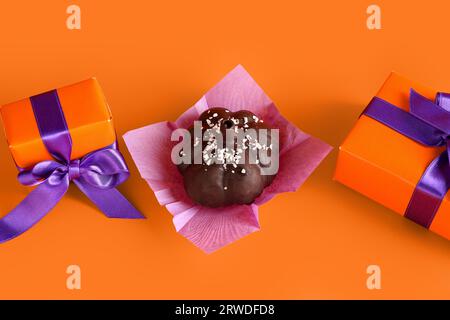 Deliziosa torta al cioccolato e confezioni regalo per festeggiare Halloween su sfondo arancione Foto Stock