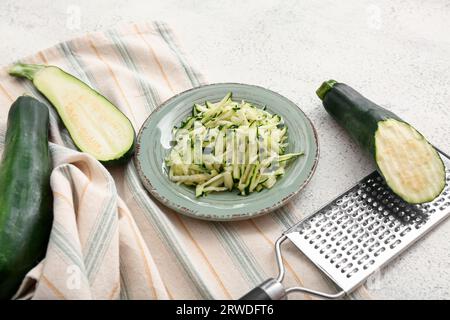 Ciotola con fette di zucchine verdi fresche e grattugia su sfondo bianco Foto Stock