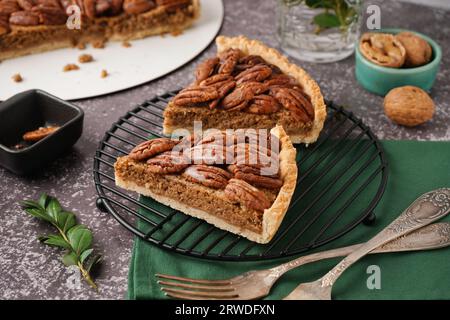 Griglia con pezzi di gustosa torta di noci pecan su sfondo grigio Foto Stock