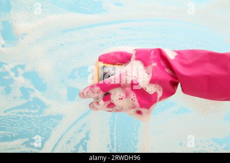 Mano femminile in guanto di gomma rosa pulizia superficie blu con spugna Foto Stock