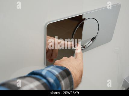 Un uomo sta premendo un muro-montato cromato lucido piatto a filo singolo per lavare la toilette. Foto Stock