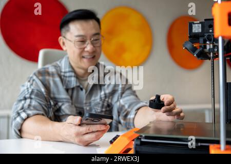 Uomo progettista che tiene in mano il rivelatore stampato su una stampante 3D che lavora in un laboratorio di ingegneria. Foto Stock