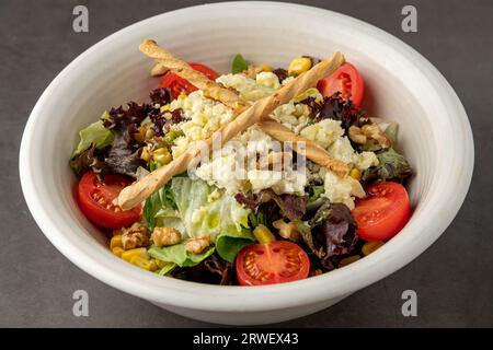 Insalata mediterranea con formaggio di capra in porcellana bianca su tavola di pietra Foto Stock