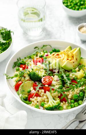 Insalata di couscous con broccoli, piselli verdi, pomodori, avocado e rucola fresca. Cibo vegetariano a base vegetale naturale sano per pranzo, cucina israeliana Foto Stock